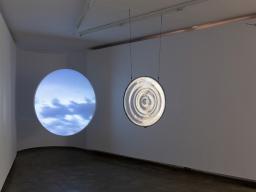 Anna May Kirk, Year Without a Sun, 2023. Volcanic sand from Mount Tambora, glass, mild steel frame, video, projector, circular projection screen (65 × 65 × 1 cm), 14 minutes 35 seconds, 2023. Photo credit Jessica Maurer. 