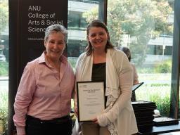 Dean of the College of Arts of Social Sciences, Bronwyn Parry presenting a framed certificate to Dr Maureen Gallagher. They are smiling and looking at the camera.