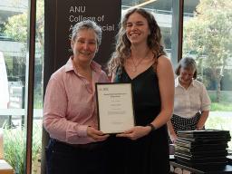 Dean of the College of Arts of Social Sciences, Bronwyn Parry presenting a framed certificate to Barbara Taylor. They are smiling and looking at the camera.