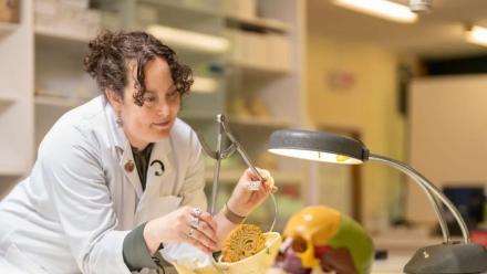 ANU PhD scholar Alannah Pearson in a lab coat, using a pair of calipers to measure the size of a model skull