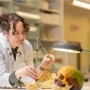 ANU PhD scholar Alannah Pearson in a lab coat, using a pair of calipers to measure the size of a model skull