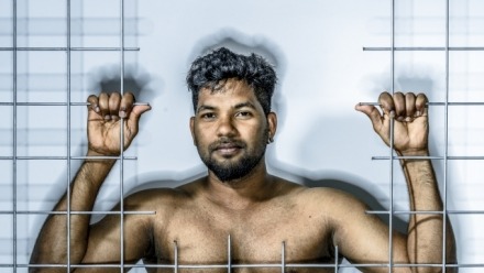 Image of a Tamil refugee, Thanush Selvarasa, standing behind bars.