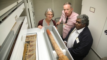 Three people examining Indigenous Australian artworks in a museum storage area