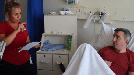 A nurse speaks with a patient who is lying in a hospital bed.